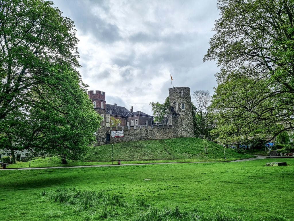Blick über eine grüne Wiese zu einer leicht erhöht stehenden Burg