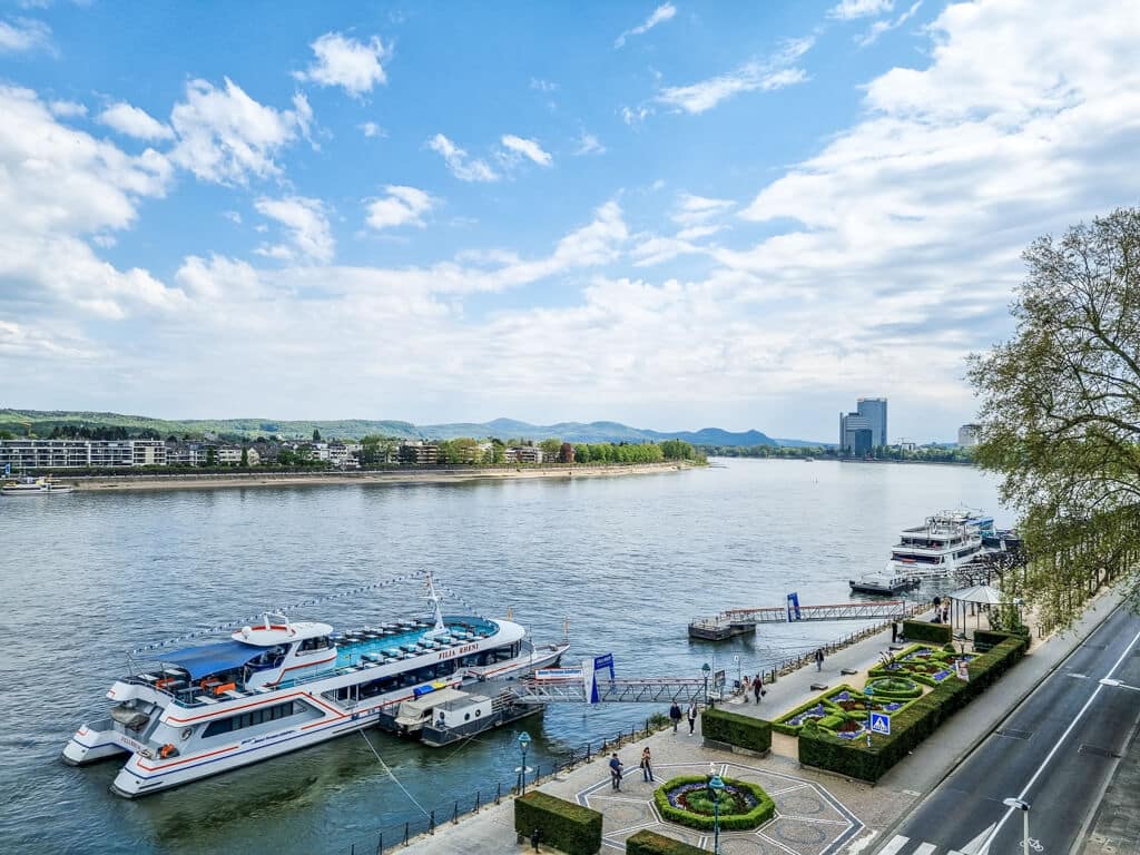 Blick über den Rhein mit einigen Ausflugsschiffen am Ufer und einer kleinen Parkanlage am Ufer