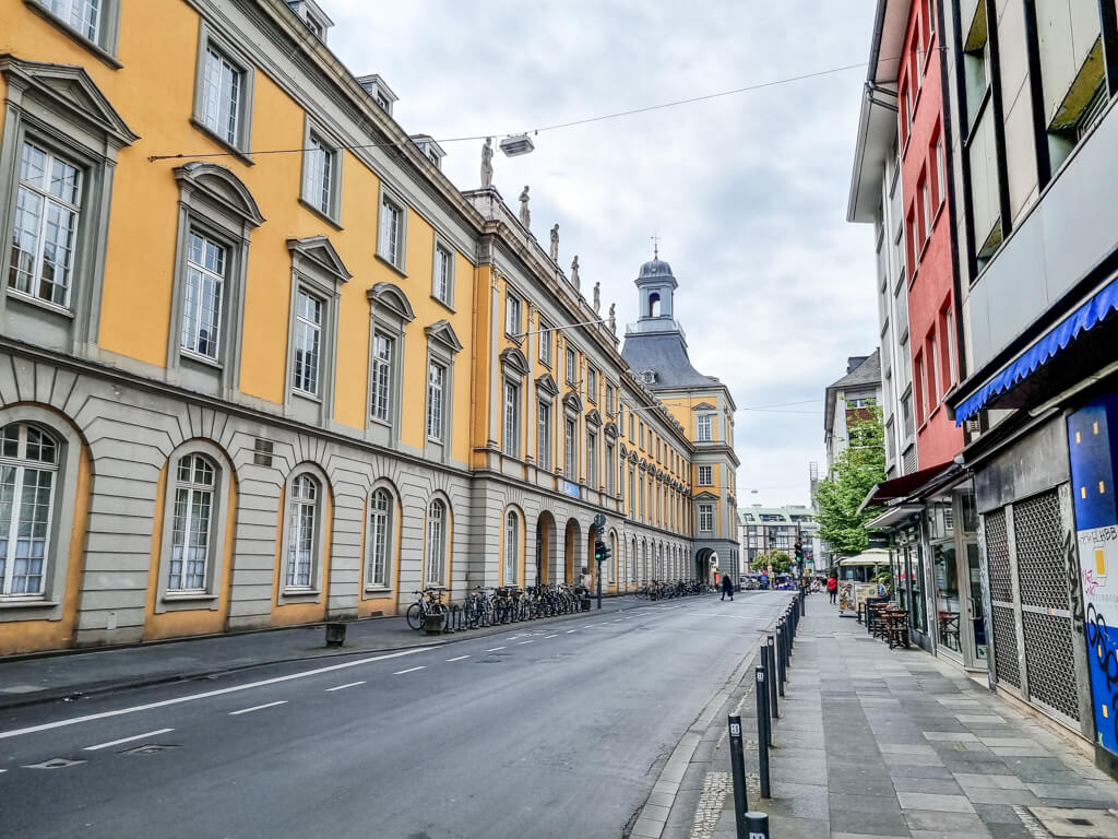 Blick über eine Straße; linksseitig das historische, langgezogene Gebäude der Universität Bonn