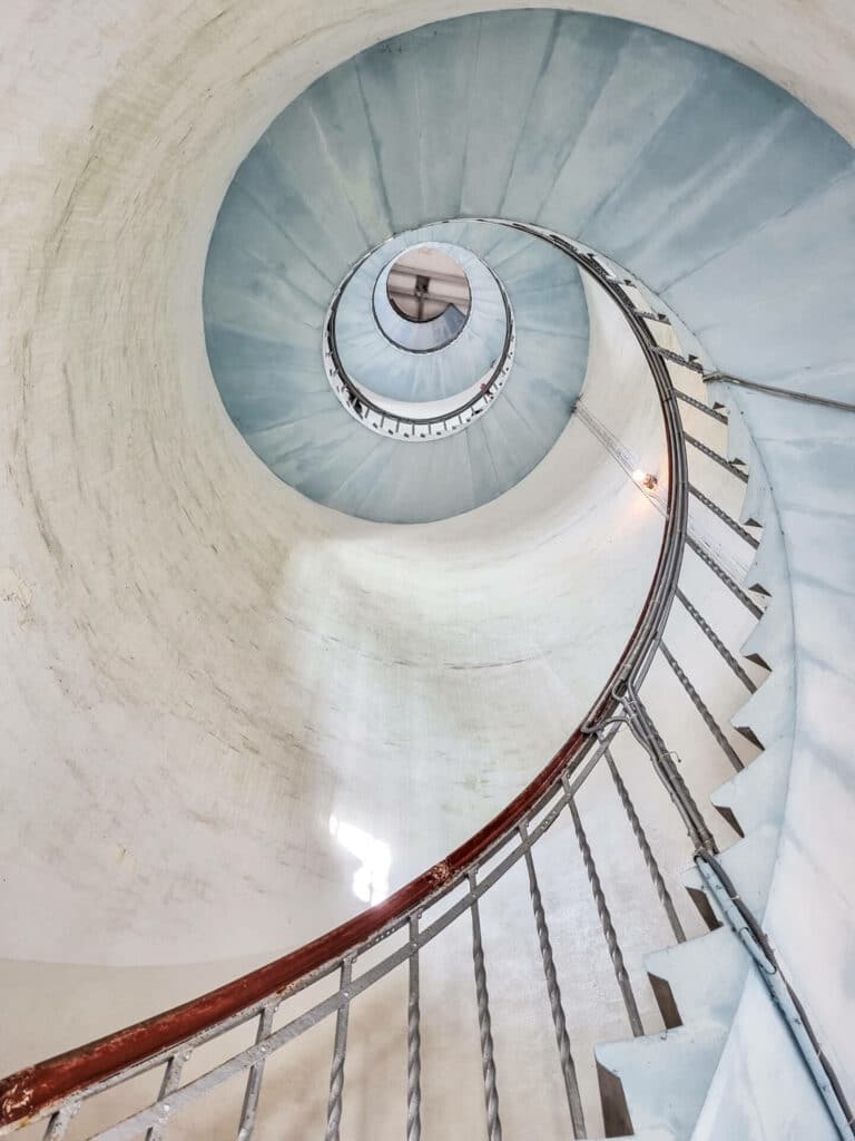schneckenförmiges Treppenhaus im Inneren eines Leuchtturm von unten fotografiert; die Treppe ist von unten hellblau gestrichen