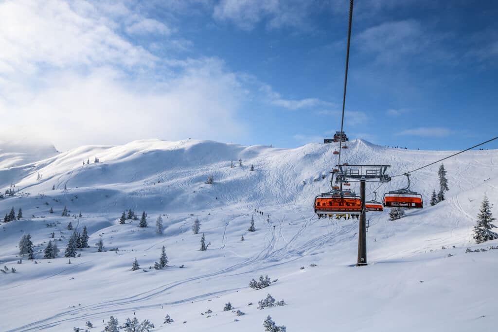 Ein Skilift mit Orangenen Hauben fährt durch die verschneiten Berge