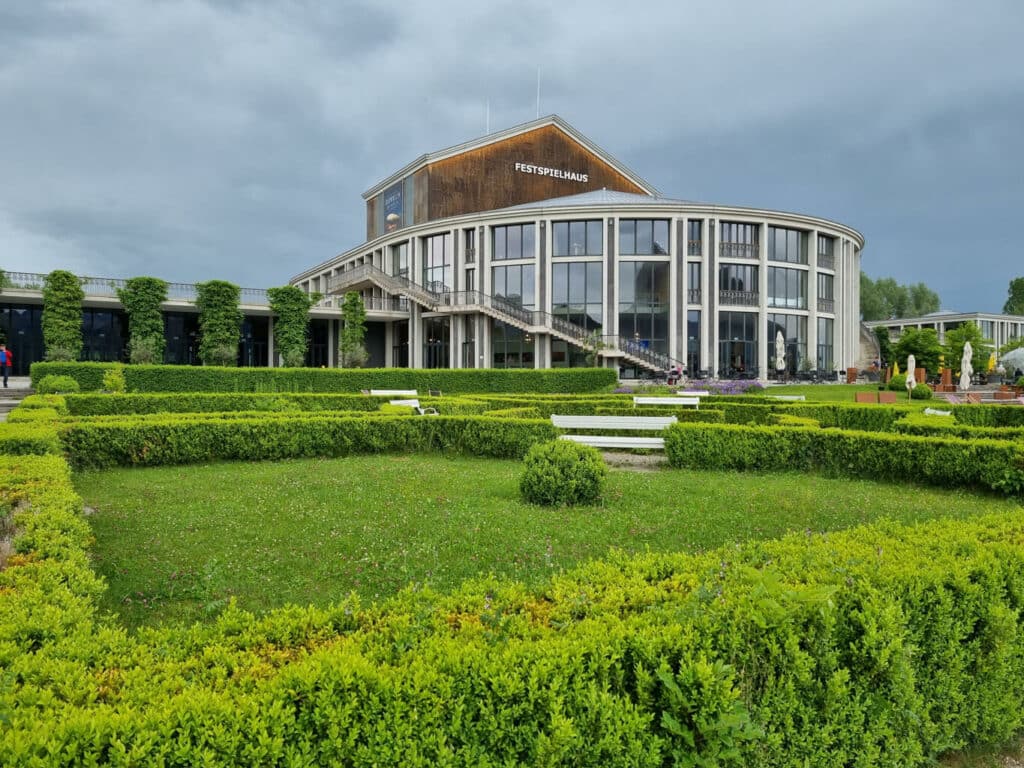 Garten mit großen Rasenflächen und niedrigen Hecken am Festspielhaus in Füssen. Das Gebäude mit der großen, gerundeten Glasfassade befindet sich im Hintergrund