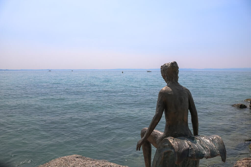 Figur einer Frau sitzt am Ufer des Gardasees