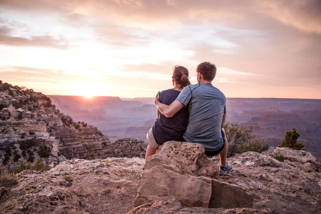 Ein Paar sitzt auf einem Stein mit Blick auf den Grand Canyon, während die Sonne untergeht