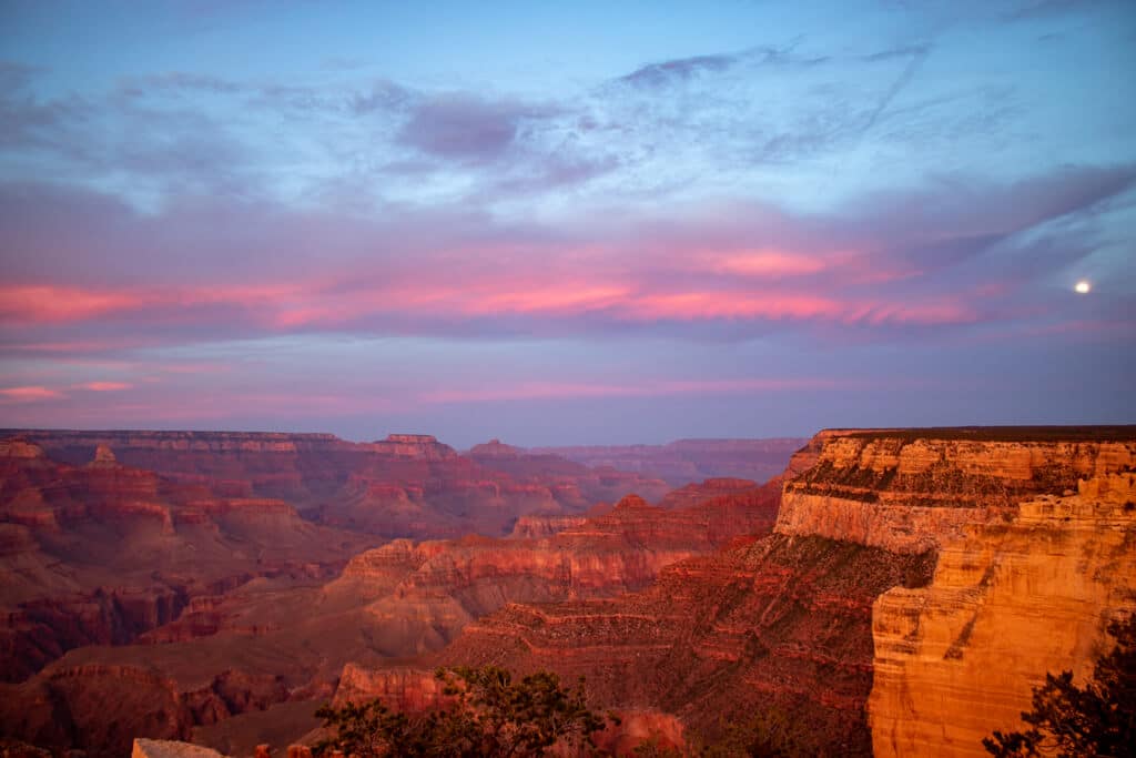Der Grand Canyon ist nach dem Sonnenuntergang in rötliches Licht getaucht und der Mond steht am Himmel