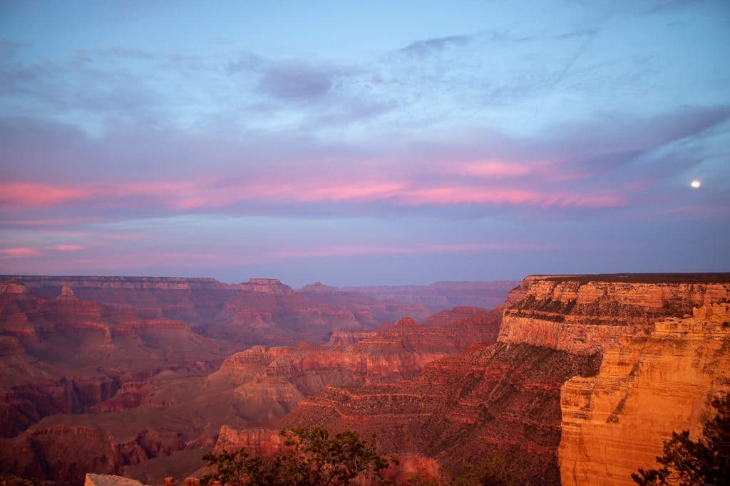 Grand Canyon - Felsen in rötliches Licht getaucht, Mond steht am Himmel