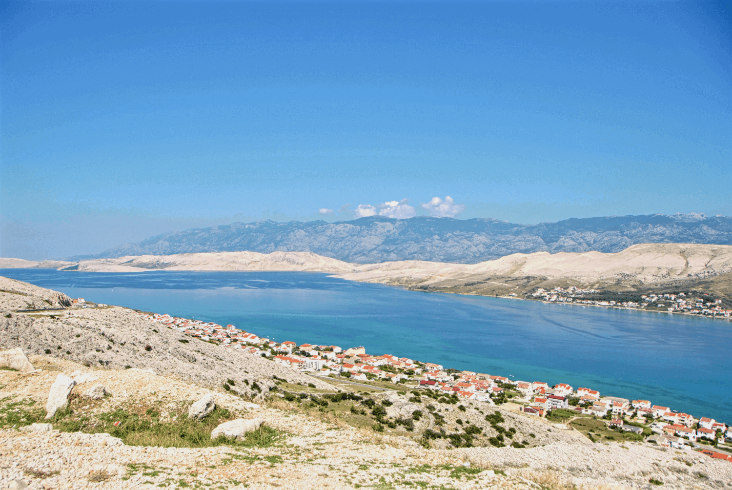 Ausblick über sanfte Hügel und ein Dorf mit dem Meer
