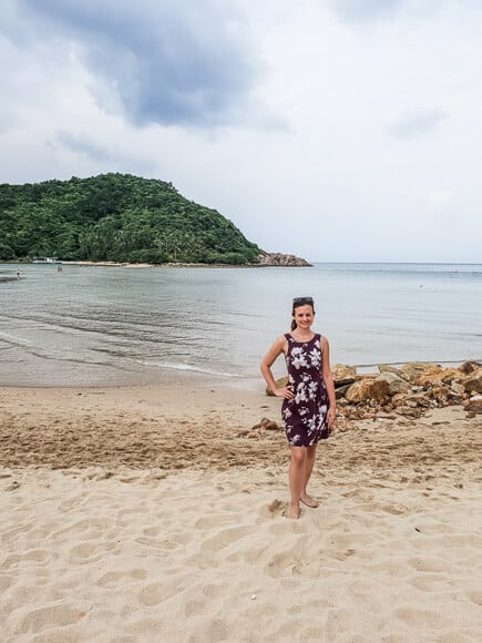 Frau steht am Strand - dahinter das Meer und eine kleine Insel