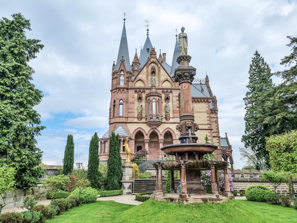 Blick über einen kleinen Garten mit einer großen Statue - dahinter liegt das Schloss Drachenburg