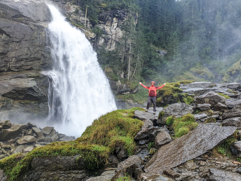 Frau posiert vor einem großen Wasserfall auf einigen moosbedeckten Steinen