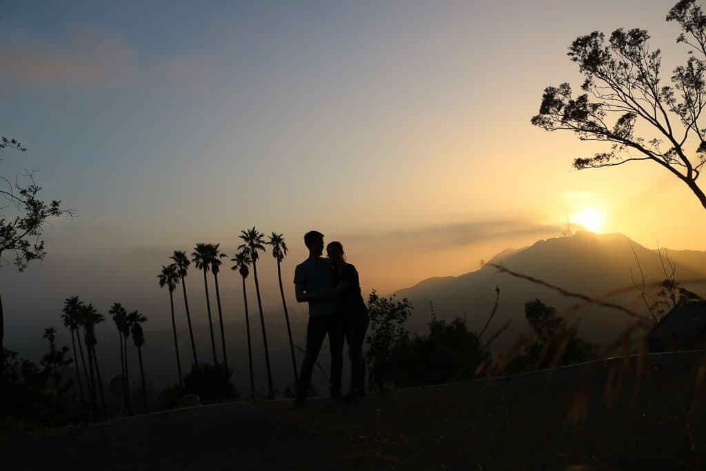 Sonnenuntergang gegenüber des Hollywood-Sign - Paar steht vor Palmen