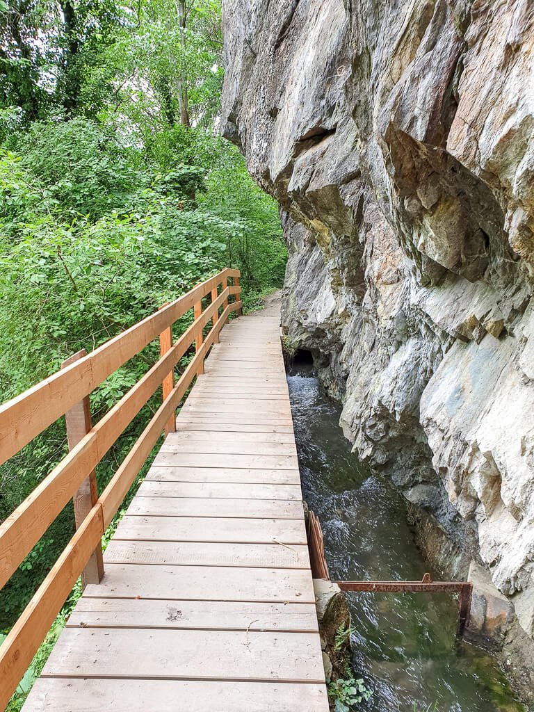 Links ein Felsen, daneben ein kleiner Fluss mit einer Holzbrücke