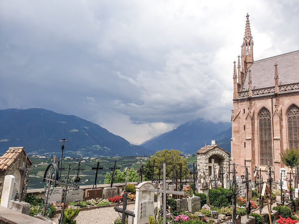 Friedhof mit Kirche und Grabsteinen, im Hintergrund Berge und dunkle Wolken