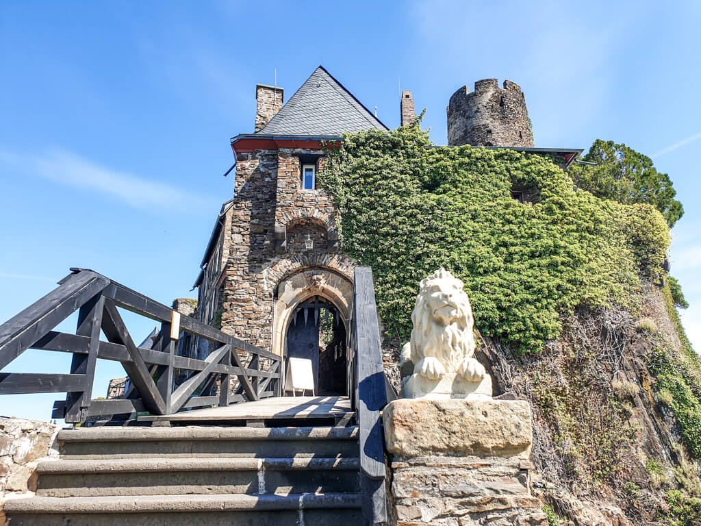 Treppe mit Holzgeländer führt zu einem Eingangstor der Burg Thurant; neben der Treppe ein steinerner Löwe