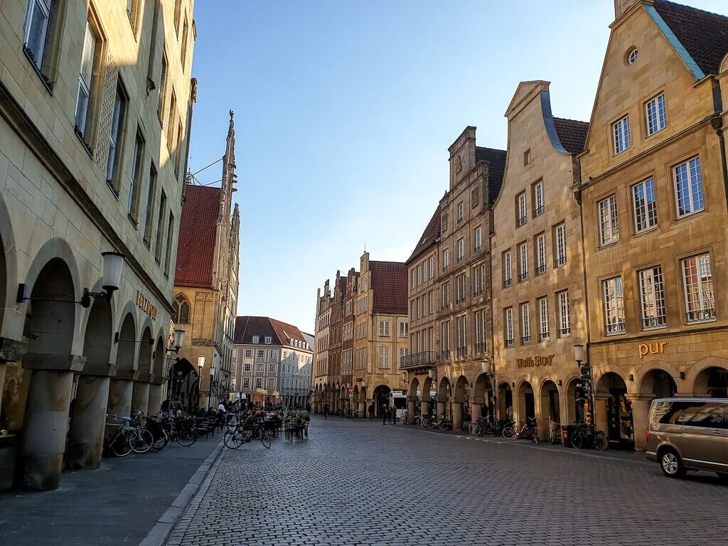 Prinzipalmarkt Münster: Innenstadt mit Kopfsteinpflaster; auf beiden Seiten befinden sich hübsche Giebelhäuser aus hellem Stein mit Bogengängen und großen Fenstern