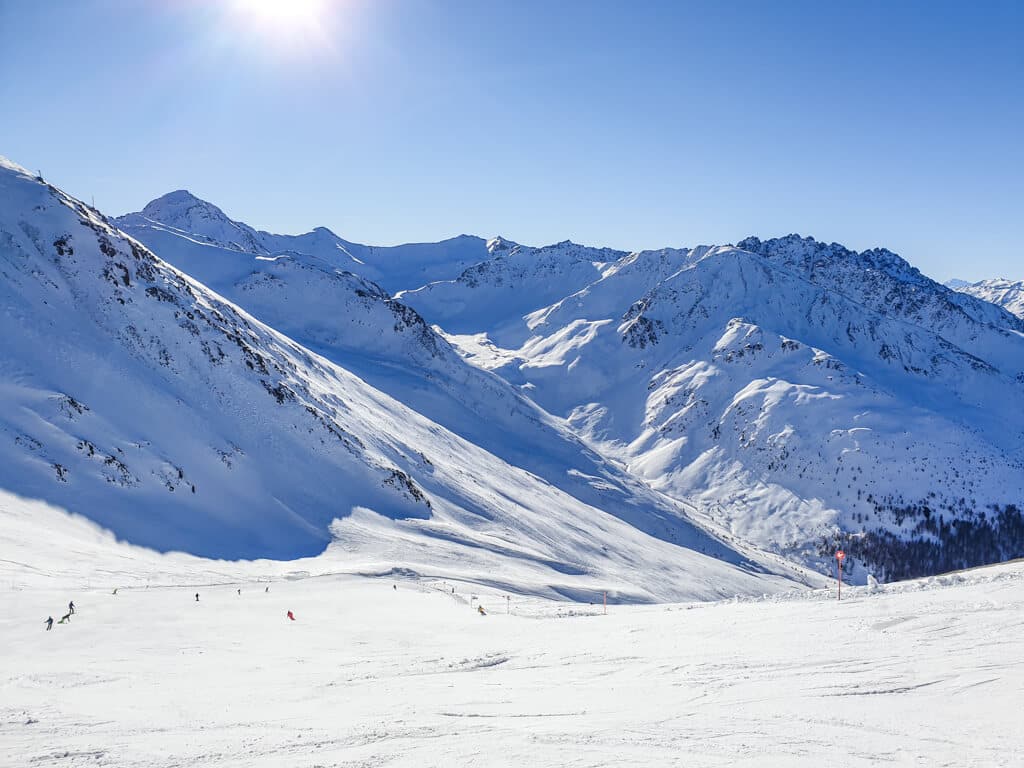 Blick hinunter an einer Skipiste mit Blick auf schneebedeckte Berge im Hintergrund