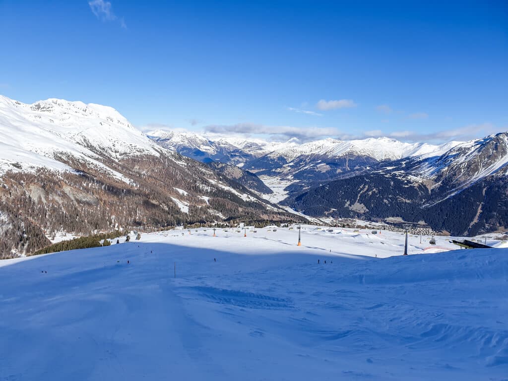 Ausblick über ein Bergpanorama mit schneebedeckten Bergen und einer Skipiste mit Sessellift im Vordergrund