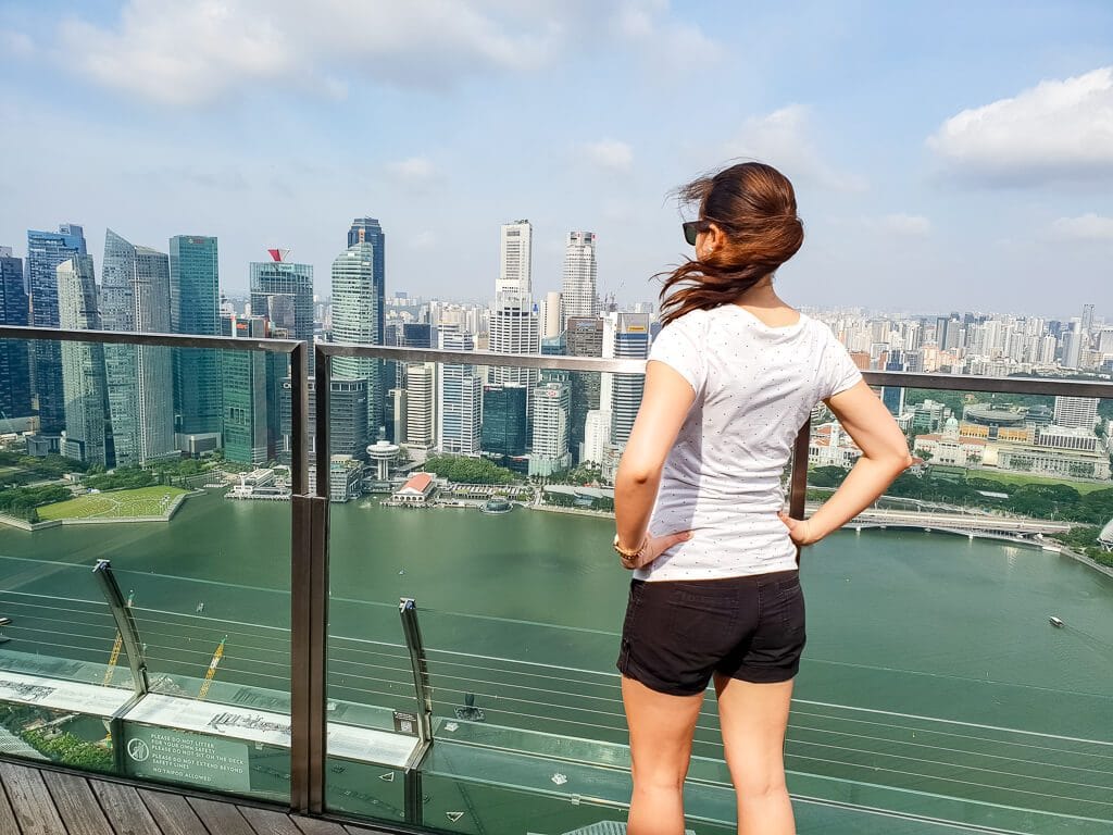 Frau steht im Wind auf Aussichtsplattform und schaut auf die Skyline von Singapur