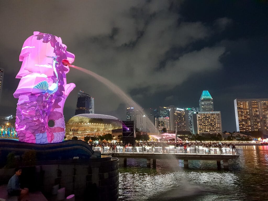 Merlion bunt angeleuchtet - dahinter die beleuchtete Skyline von Singapur