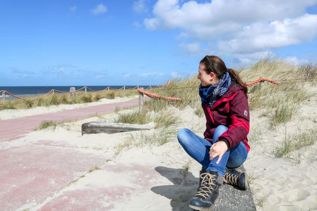 Frau sitzt auf einer Bank in den Dünen und schaut aufs Meer