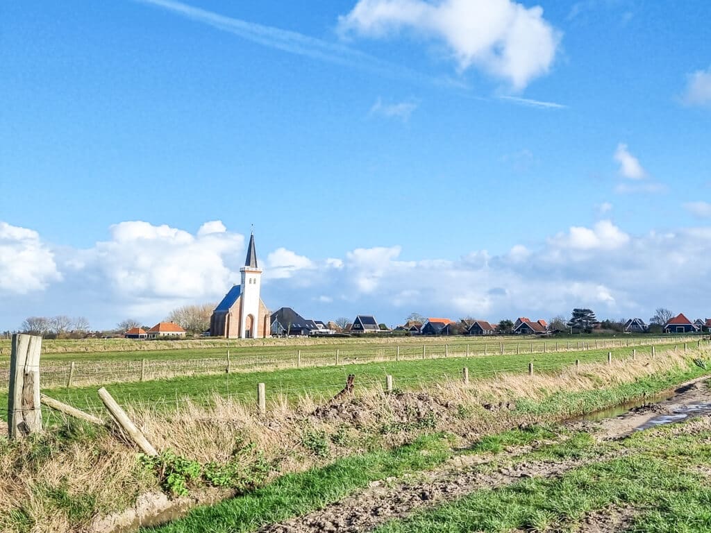 Blick über ein grünes Feld auf eine Kirche mit weißem Turm und einige Häuser 