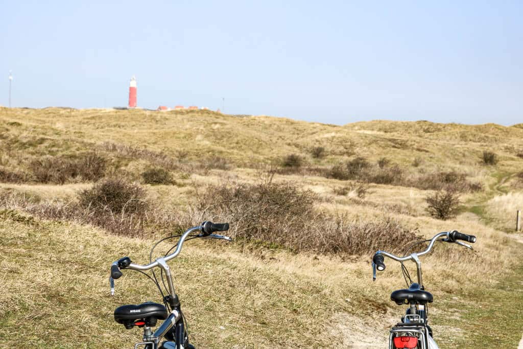 zwei Fahrräder stehen in einer Graslandschaft - im Hintergrund ein roter Leuchtturm