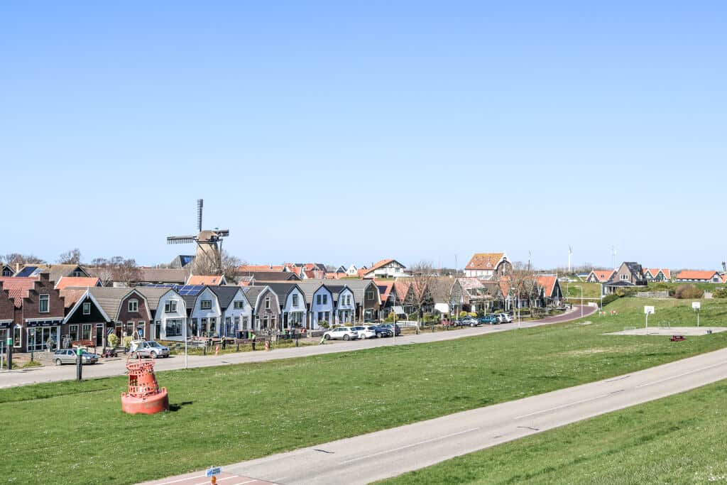 Blick auf eine Häuserreihe und eine Windmühle vom Deich aus