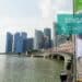 Brücke mit Fahnen, links Wasser und im Hintergrund die Skyline von Singapur