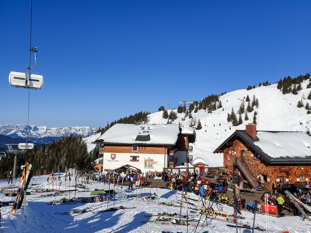 zwei Häuser in den Bergen, davor viele abgestellte Skier