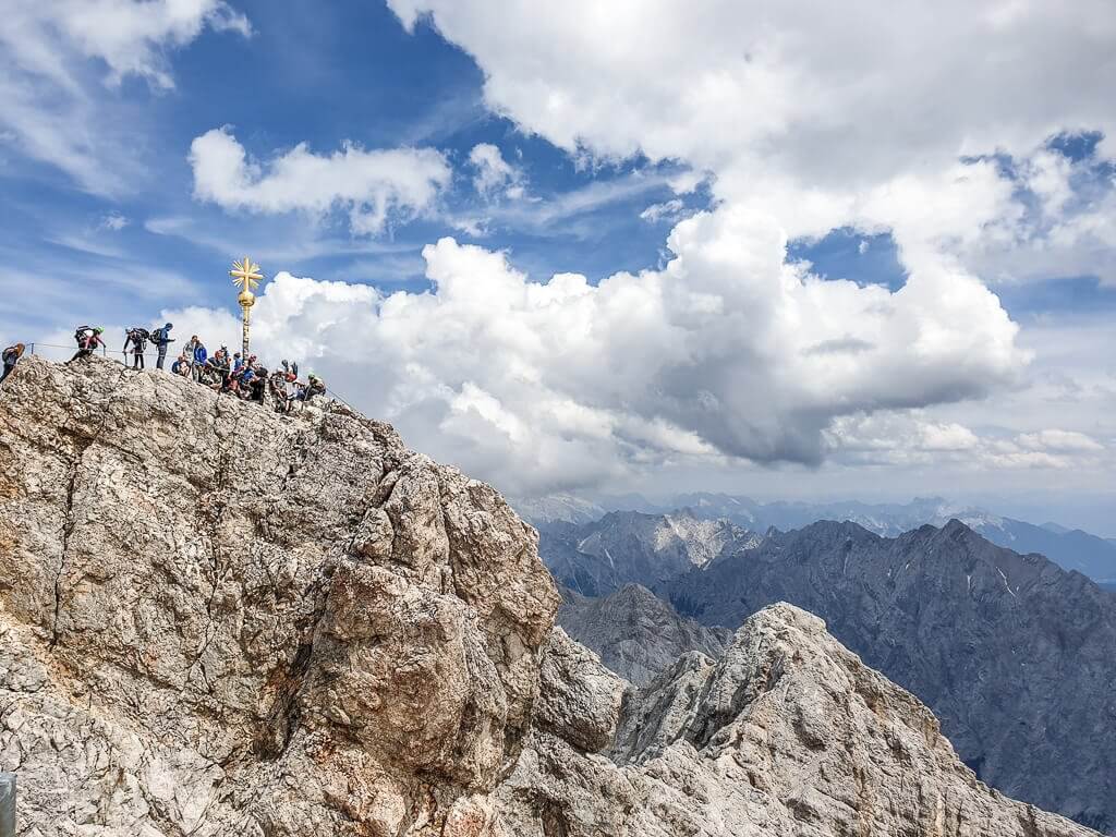 Zugspitze, goldenes Gipfelkreuz auf dem Felsen mit vielen Menschen drumherum